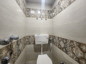 A bathroom with a toilet, a sink, and a shower area. - Hotel The Divine (New Delhi)
