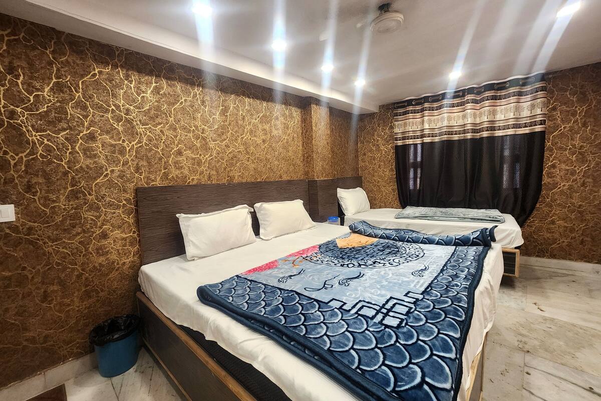 Ein Hotelzimmer mit einem großen Bett, einem kleineren Bett und einem Nachttisch. Die Wände sind strukturiert und die Decke verfügt über eingelassene Beleuchtung.