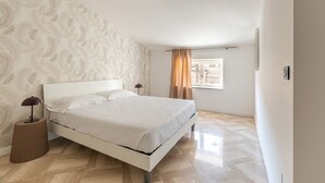 A bedroom with a bed, a nightstand, a lamp, a window with curtains, and a patterned wall.