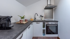A compact kitchen with a modern stove, a built-in oven, a stainless steel range hood, and a black coffee machine.