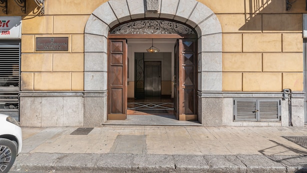 A building entrance with a stone archway, a wooden door, and a metal gate.
