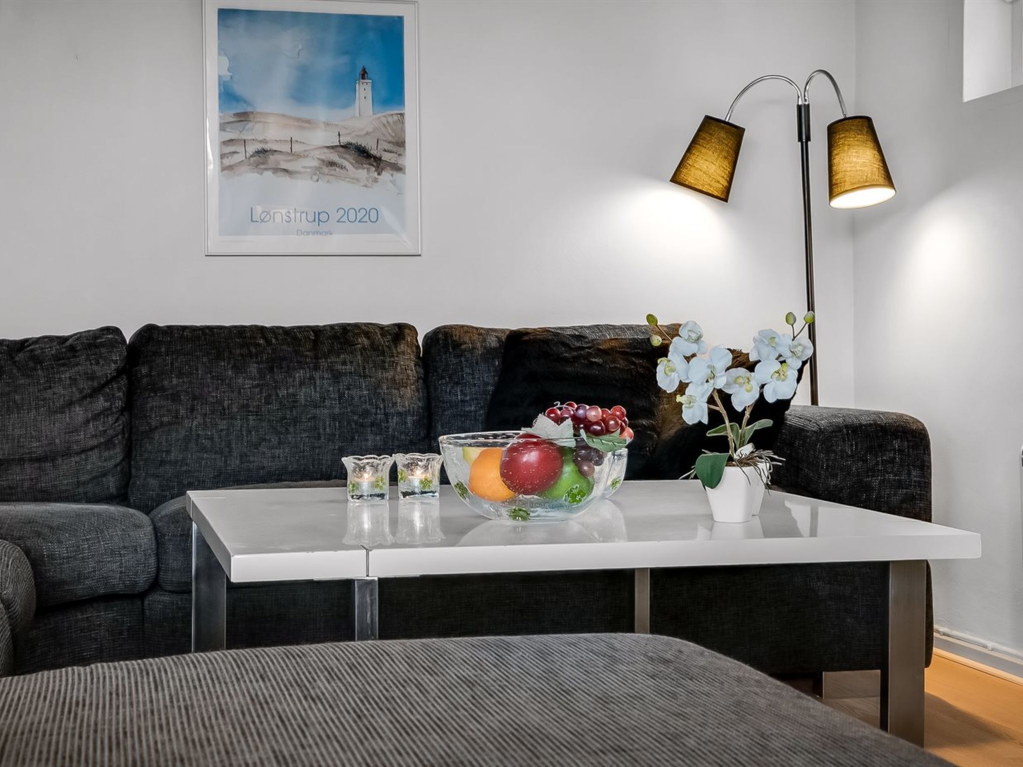 A modern living room with a white coffee table, a bowl of fruit, a potted orchid, and a floor lamp.