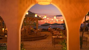 An outdoor restaurant with tables and chairs, umbrellas, and a view of the ocean at sunset. - Living Asia Sunset Resort (Gili Air)