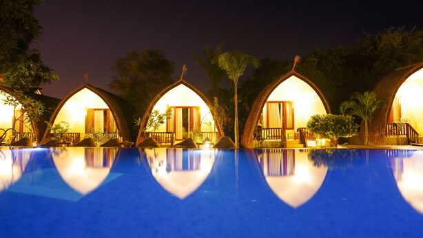 A pool with four dome-shaped cottages, each with a door and windows, surrounded by trees. - Living Asia Sunset Resort (Gili Air)