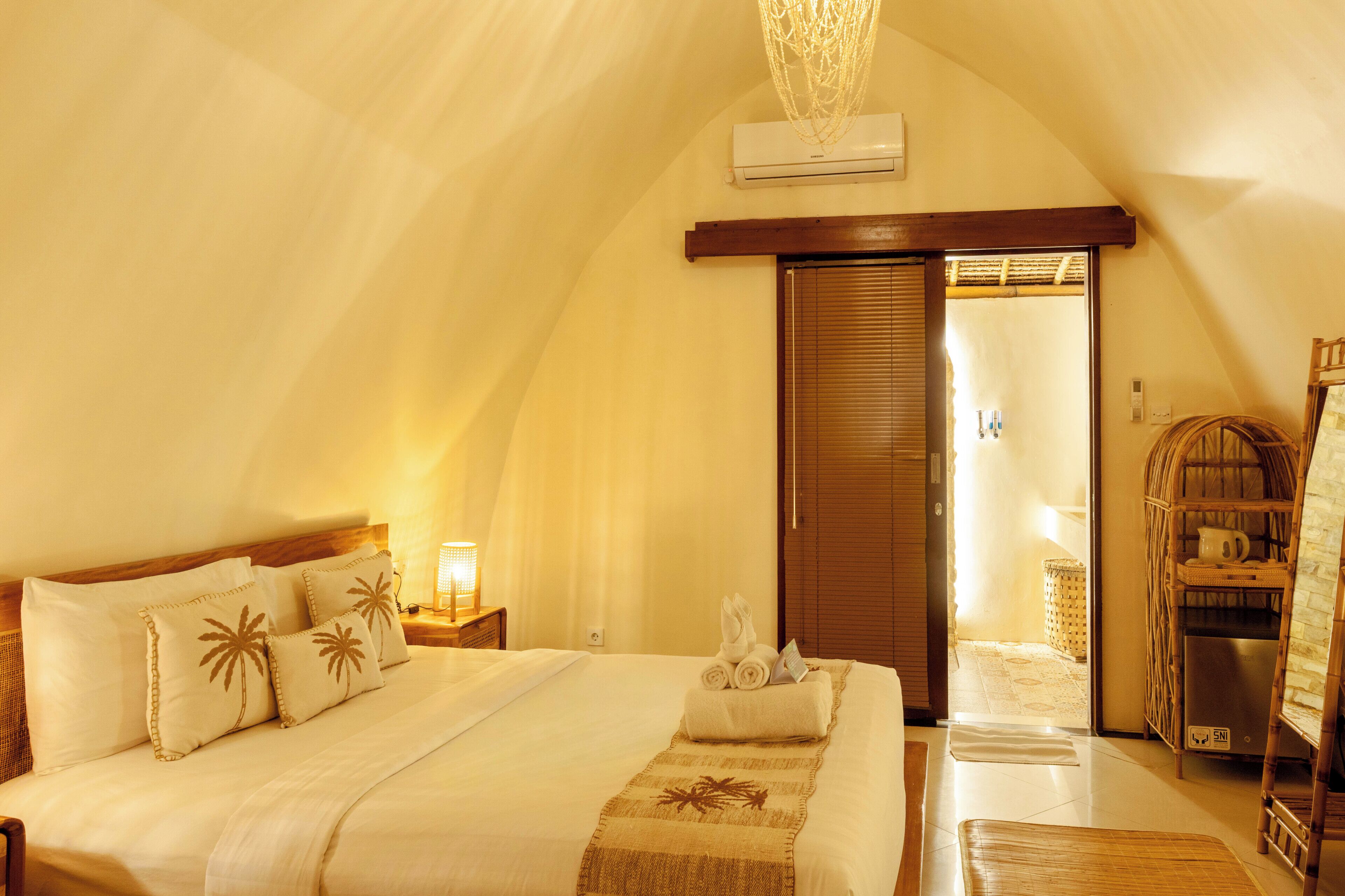 A bedroom with a bed, a nightstand, a lamp, a towel, and a door leading to another room.
