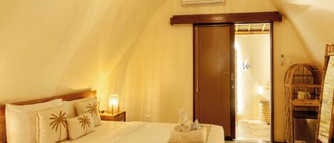 A bedroom with a bed, a nightstand, a lamp, a towel, and a door leading to another room.