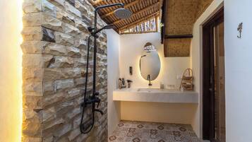 A bathroom with a stone wall, a shower, a sink with a mirror, and patterned tiles.