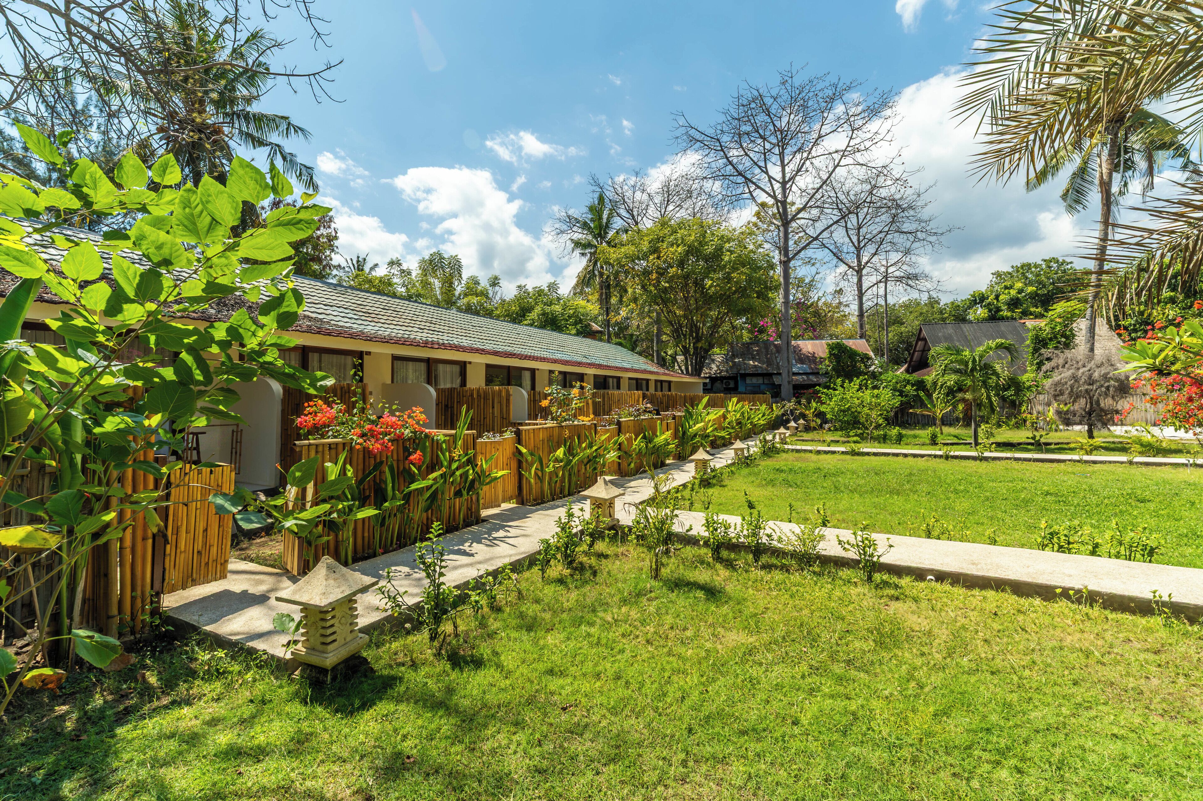 A hotel with a row of rooms, a garden with various plants, and a clear sky.