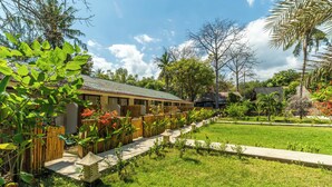 A hotel with a row of rooms, a garden with various plants, and a clear sky. - Living Asia Sunset Resort (Gili Air)