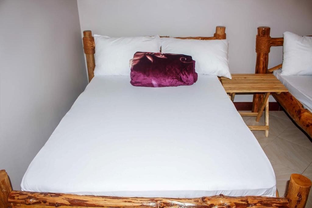 Ein Einzelbett mit Holz-Kopf- und Fußteil, eine Holzbank und ein lilanes Kissen.