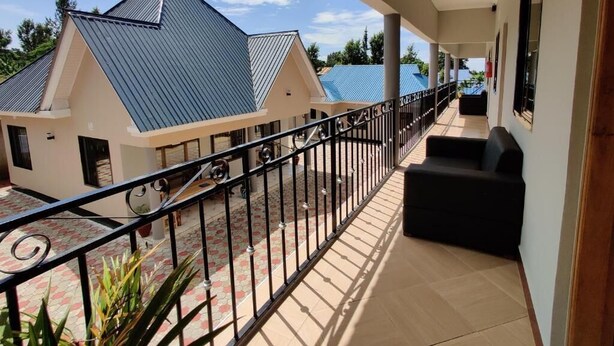 Un balcon couvert avec une balustrade, un canapé et une vue sur deux immeubles aux toits bleus.