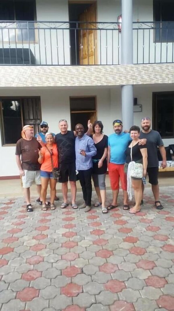A group of people standing in front of a building with a tiled patio and a balcony. - Wanyama Hostel (Arusha)