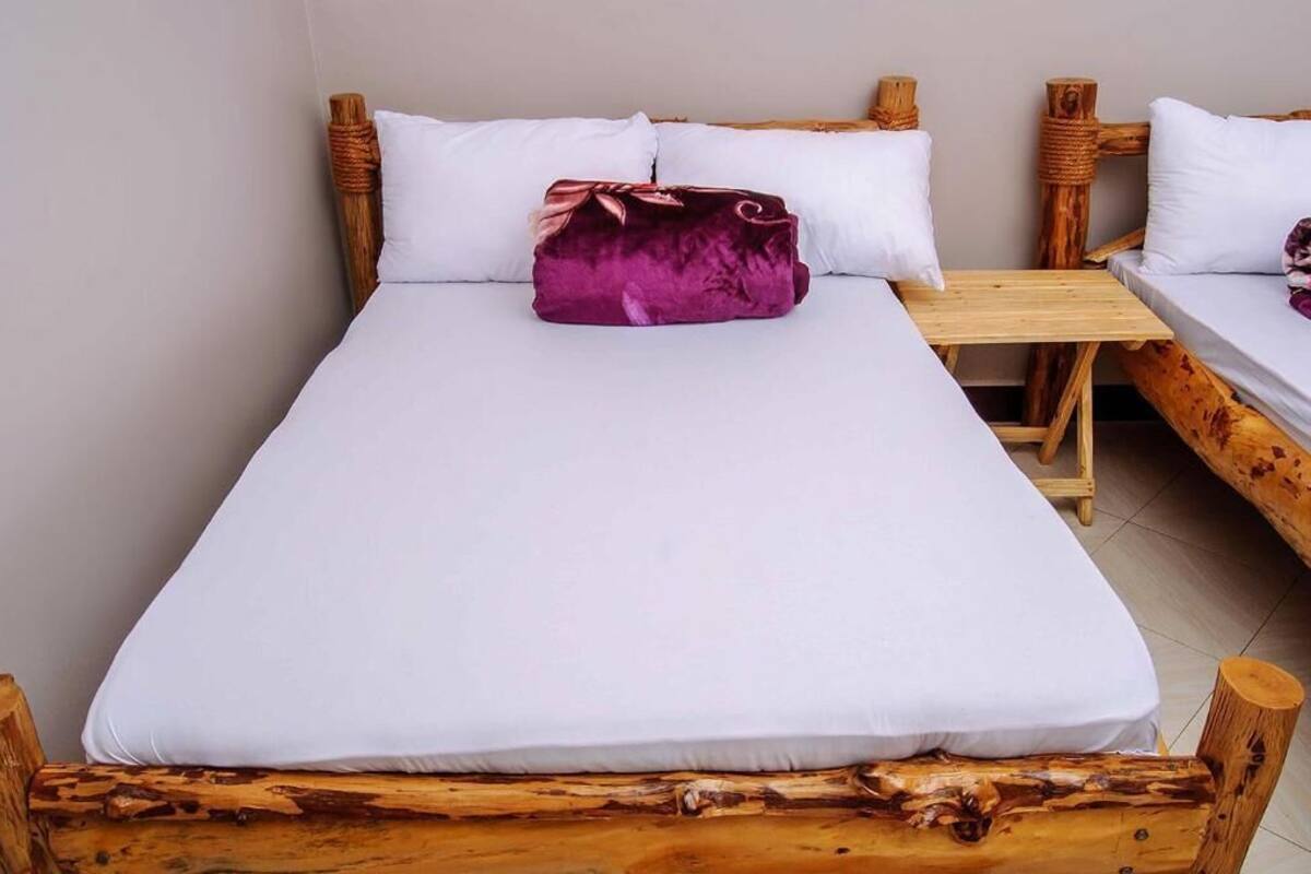 A bed with white bedding and a purple pillow, wooden headboard, and a wooden table beside it.