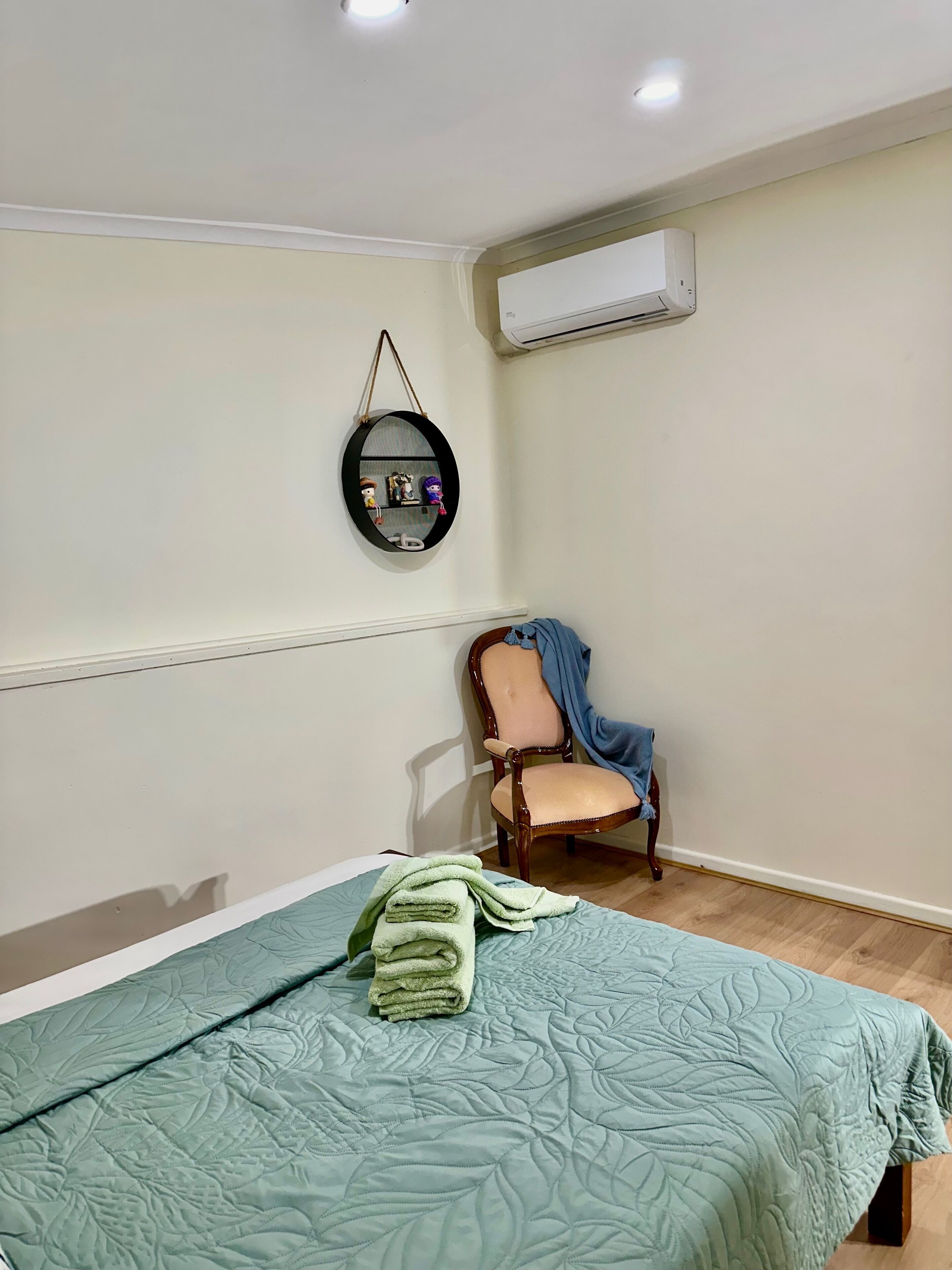 A room with a bed, a chair, a wall-mounted shelf, and an air conditioning unit.