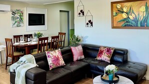 A modern living room with a black leather sofa, two round tables, and a dining area with wooden chairs and a TV. - Woodville Garden Home in great location (Woodville Gardens)