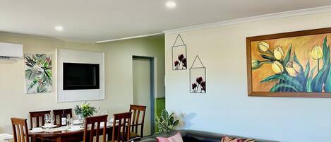 A modern living room with a black leather sofa, two round tables, and a dining area with wooden chairs and a TV.