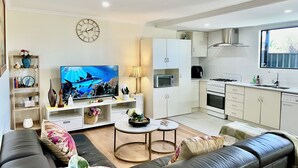 A modern living room with a flat-screen TV, sofa, coffee table, and a kitchen area with cabinets, microwave, and stove. - Woodville Garden Home in great location (Woodville Gardens)