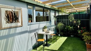 A covered patio with a table and chairs, surrounded by potted plants and a fenced garden area. - Woodville Garden Home in great location (Woodville Gardens)
