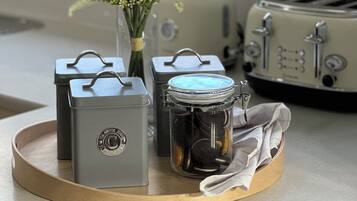 Un comptoir de cuisine sur lequel se trouve un plateau avec une théière, un bocal de biscuits et un vase rempli de fleurs.