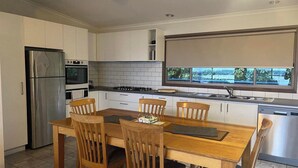 A modern kitchen with white cabinets, a stainless steel refrigerator, a gas stove, and a window with a view of the outdoors. - 12 Raheen Drive, Mallacoota (Mallacoota)