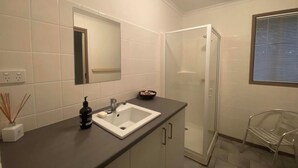 A modern bathroom with a white sink, mirror, and shower. - 12 Raheen Drive, Mallacoota (Mallacoota)