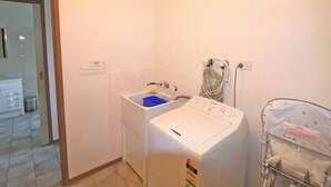 A laundry area with a washing machine, a sink, and a drying rack. - 12 Raheen Drive, Mallacoota (Mallacoota)