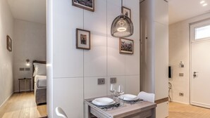 Un comedor con una mesa de madera dispuesta para dos personas, sillas blancas y una lámpara colgante.