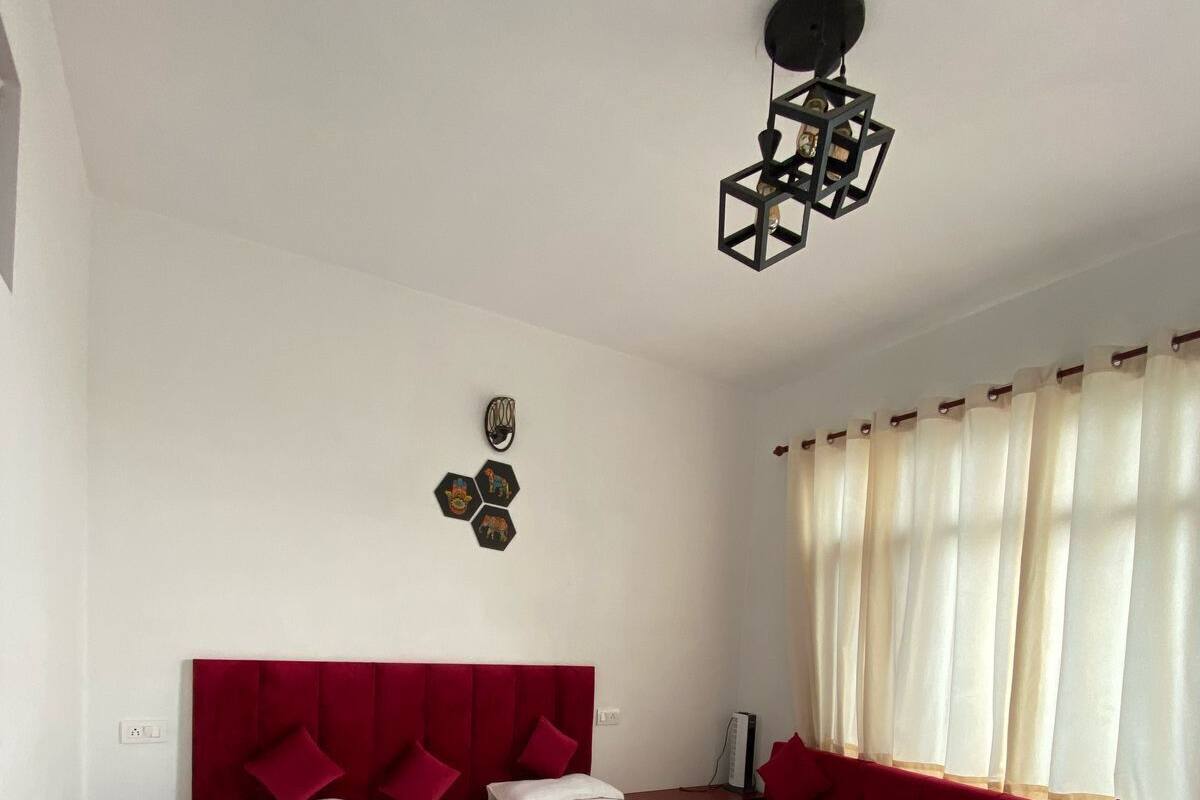 A bedroom with a large bed, a red sofa, a patterned rug, and a wall-mounted light fixture.