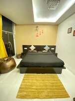 A bedroom with a bed, a brown rug, a yellow curtain, and a chandelier.
