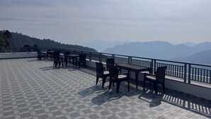 A terrace with tables and chairs, offering a view of distant mountains. - Cozy Kanatal Hotel And Resort (Tehri)