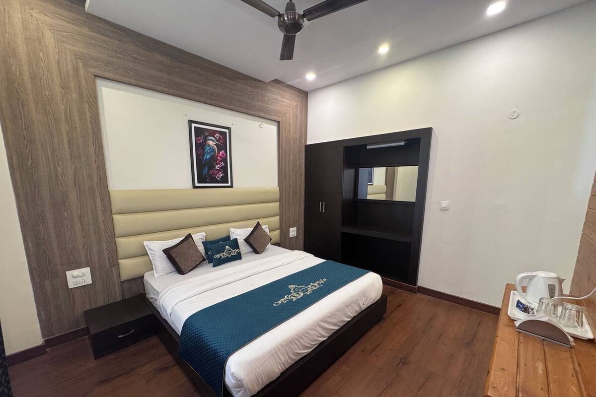 Ein modernes Hotelzimmer mit einem großen Bett, einem Holzkopfende, einem eingebauten Fernseher, einem kleinen Tisch mit Wasserkocher und einem Deckenventilator.