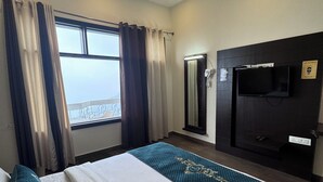 A hotel room with a bed, a ceiling fan, a TV, and a window with curtains. - Cozy Kanatal Hotel And Resort (Tehri)