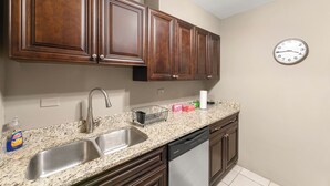 A kitchen with wooden cabinets, a stainless steel sink, and a clock on the wall.