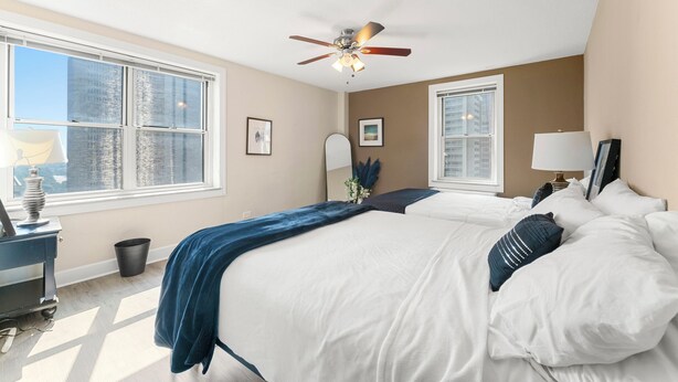 A bedroom with a large bed, a ceiling fan, and two windows.
