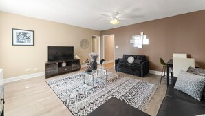 A living room with a flat-screen TV, a black sofa, a coffee table, and a patterned rug.