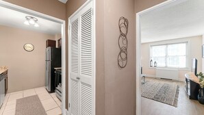 A modern kitchen with white cabinets, a refrigerator, and a stove. There is a clock on the wall and a window with blinds.