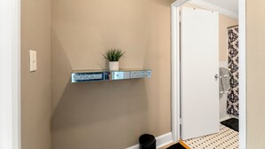 A hallway with a beige wall, a white door, a small plant on a shelf, and a black trash can.