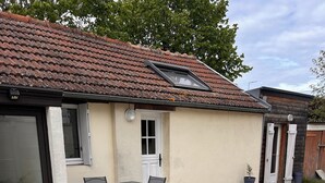 A house with a tiled roof, a small patio with a table and chairs, and a gravel driveway.