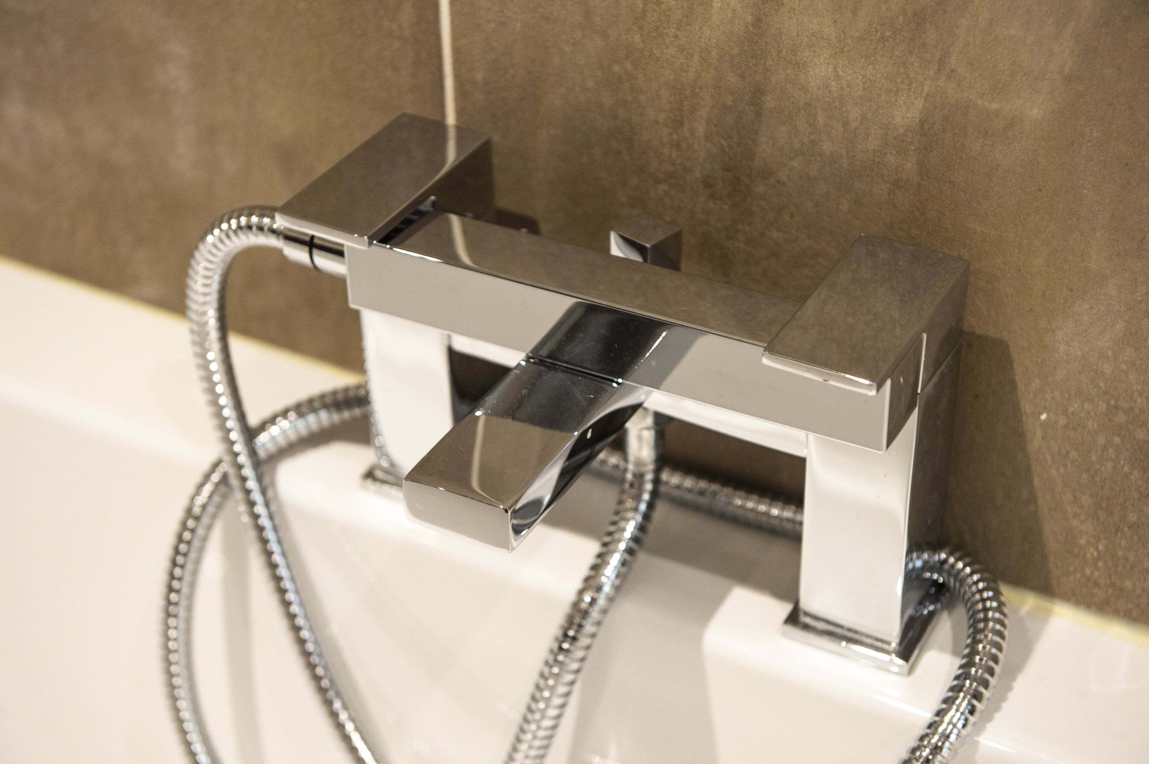 A modern bathroom with a chrome faucet and shower hose.