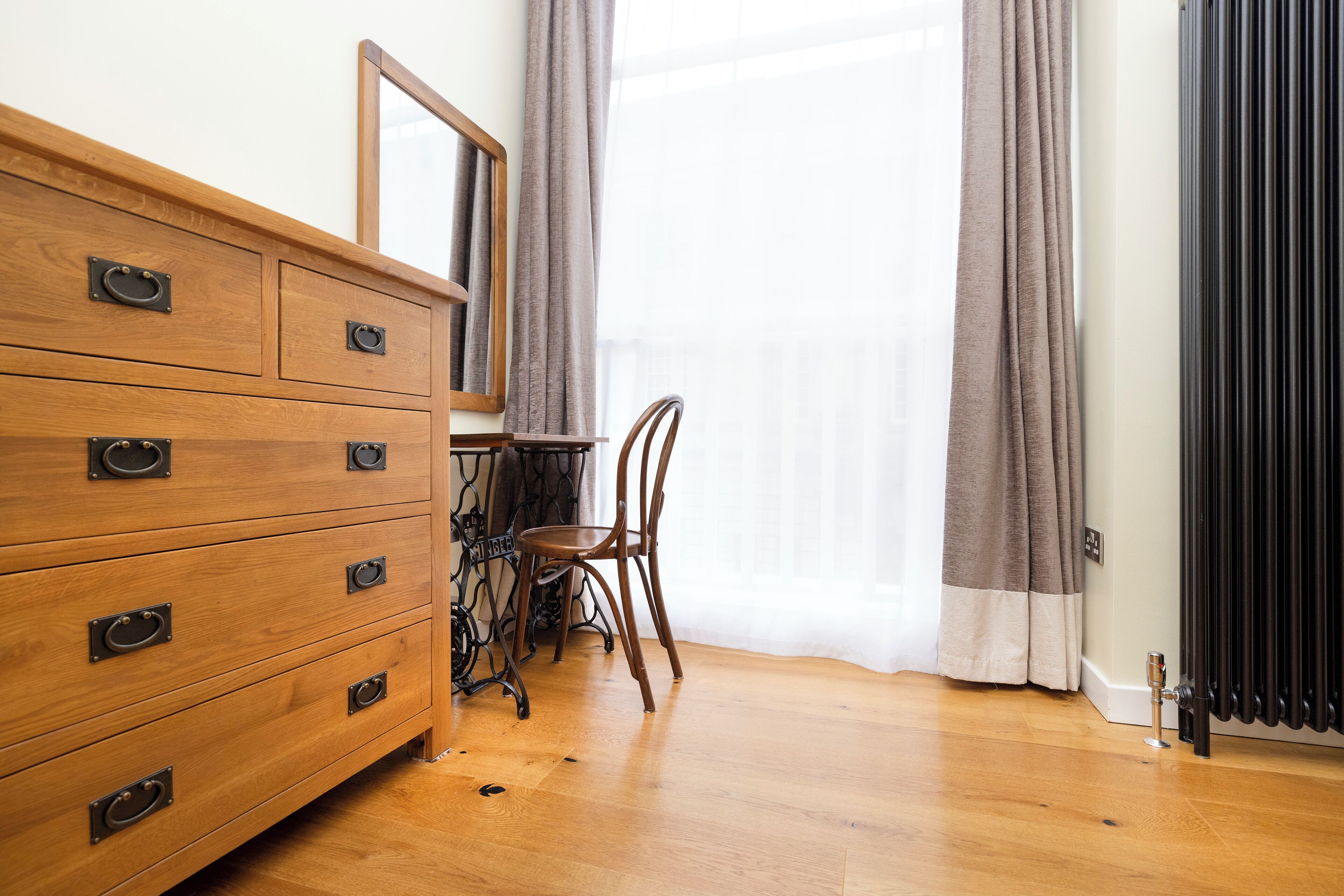 A wooden dresser with multiple drawers, a chair, a table, and a radiator.