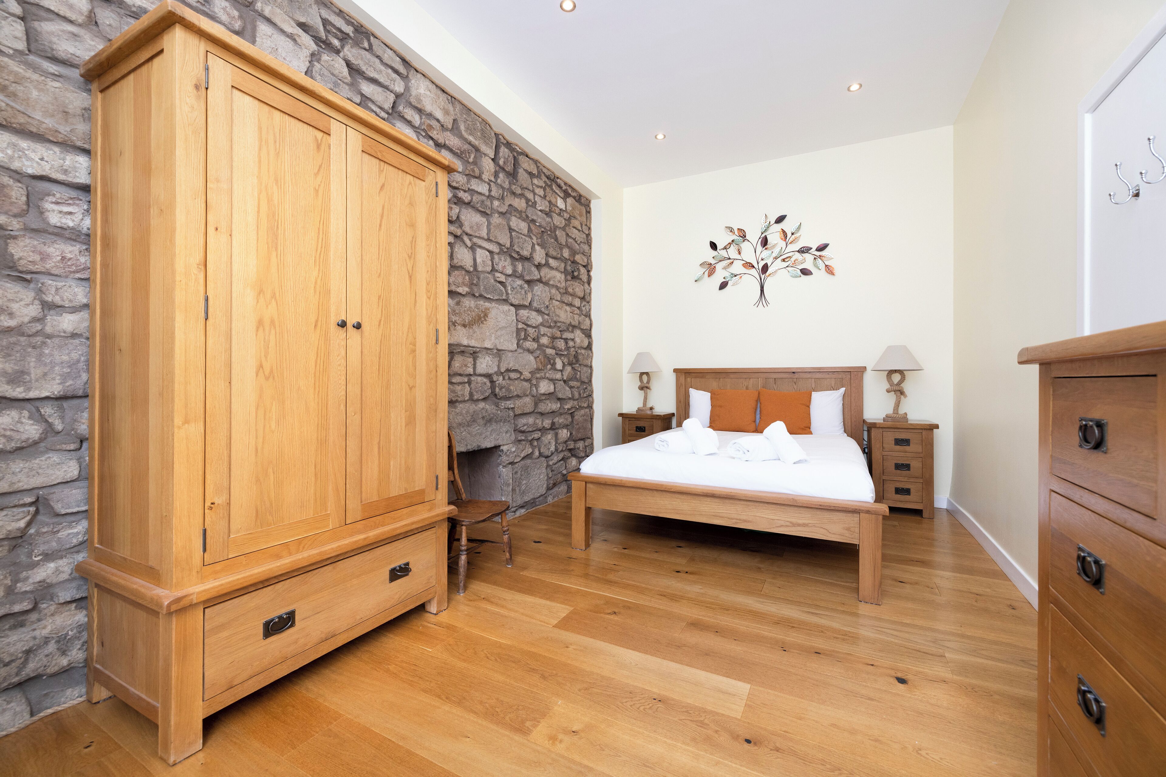 A bedroom with a stone wall, wooden wardrobe, bed, nightstands, and a dresser.