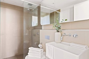 A modern bathroom with a glass shower enclosure, a white sink with a towel rack, and a mirror above the sink.