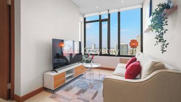 A modern living room with a large TV, a sofa, a coffee table, and a view of the city through large windows.