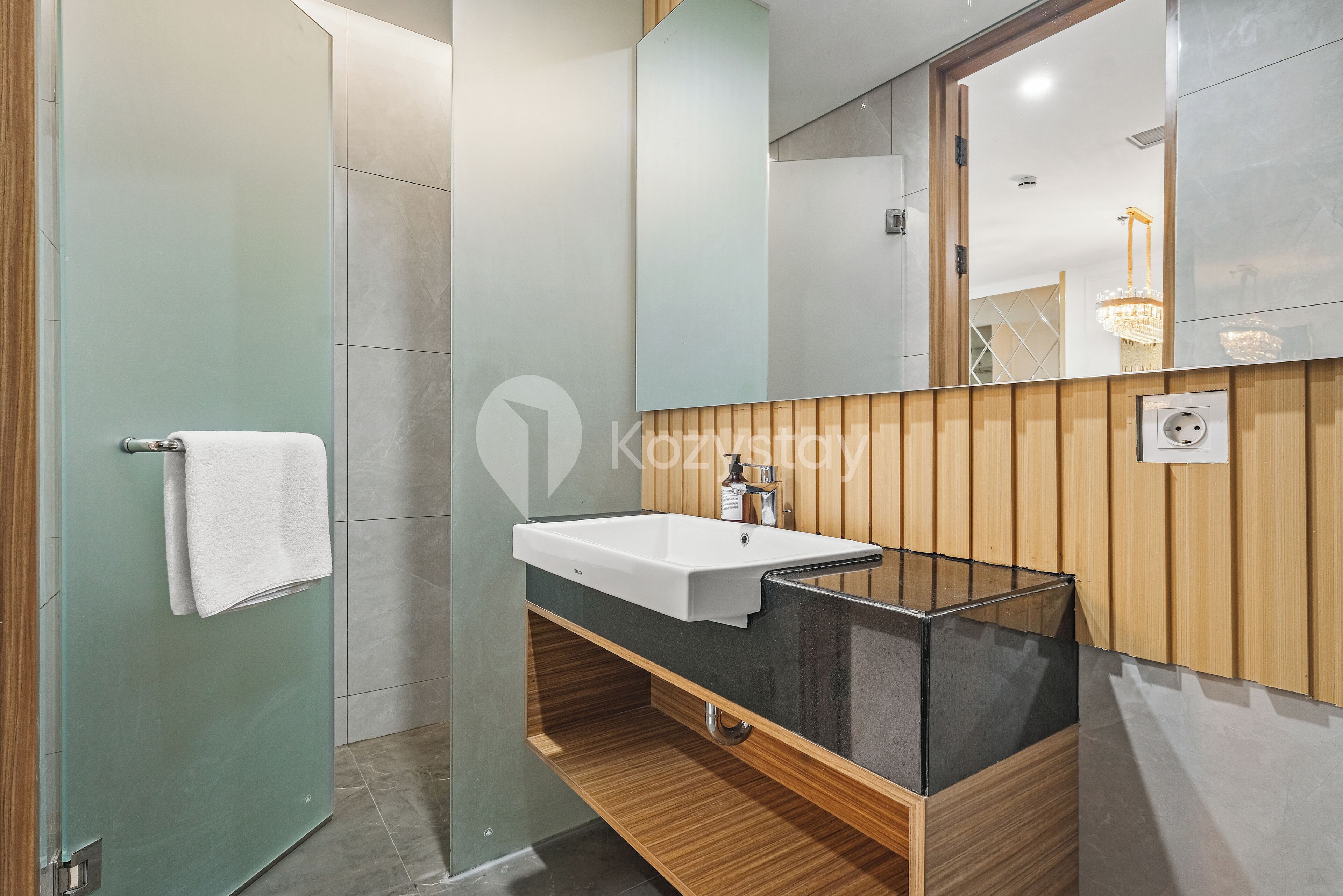 A modern bathroom with a glass shower enclosure, a wooden vanity with a white sink, and a large mirror.