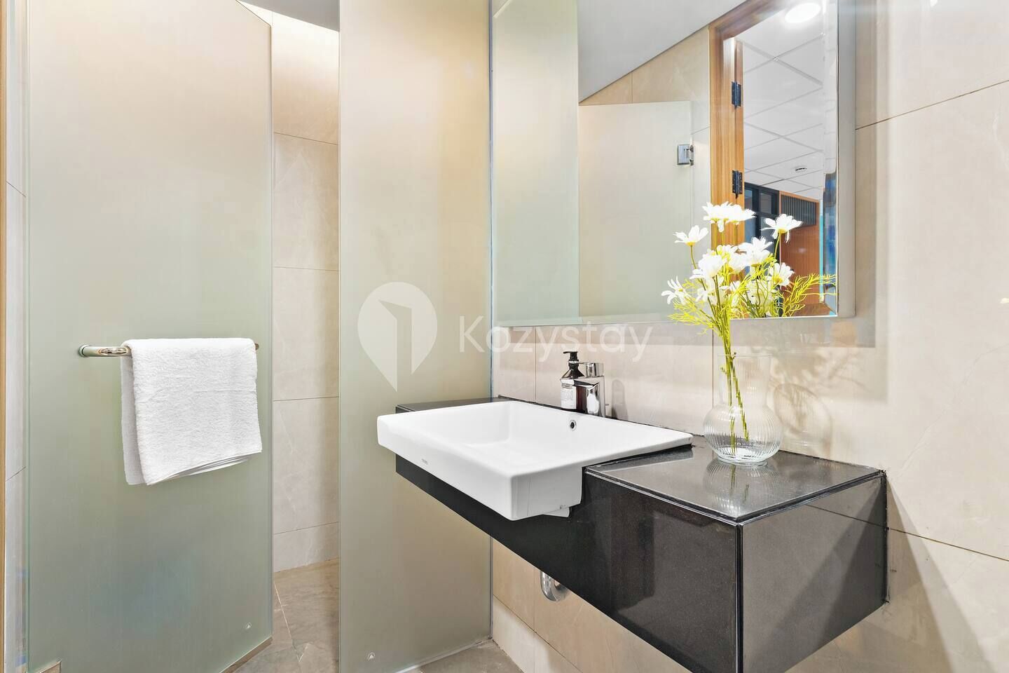 Un baño moderno con lavamanos blanco, tocador negro y cabina de ducha de vidrio.