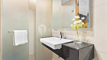 Un baño moderno con lavamanos blanco, tocador negro y cabina de ducha de vidrio.