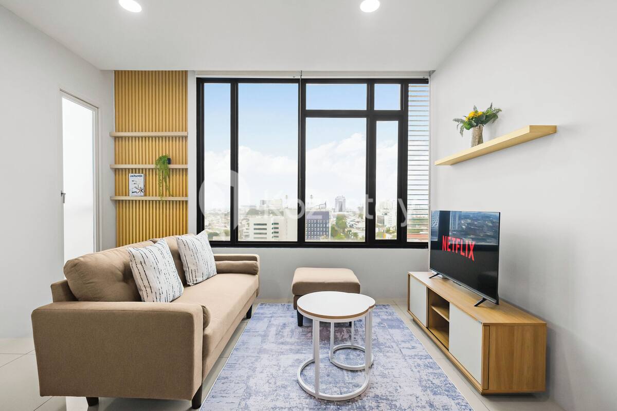 Una sala de estar moderna con un sofá, una mesa de centro, un televisor sobre un mueble de madera y un ventanal con vistas a la ciudad.