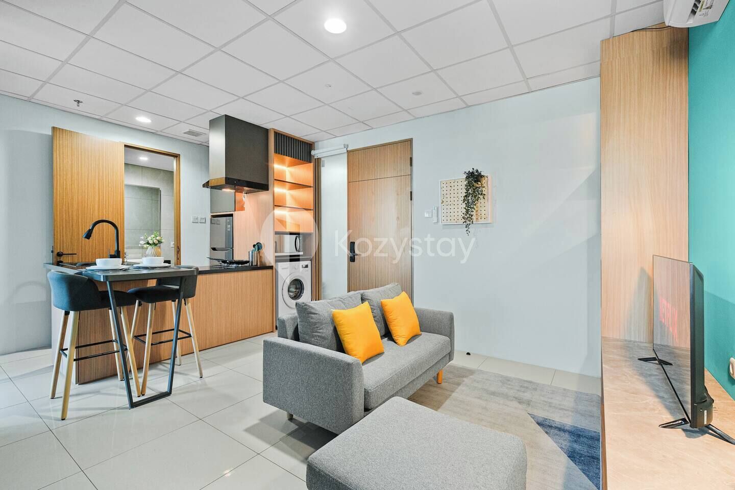 A compact living space with a kitchenette, a sofa with cushions, a small dining area, and a TV.