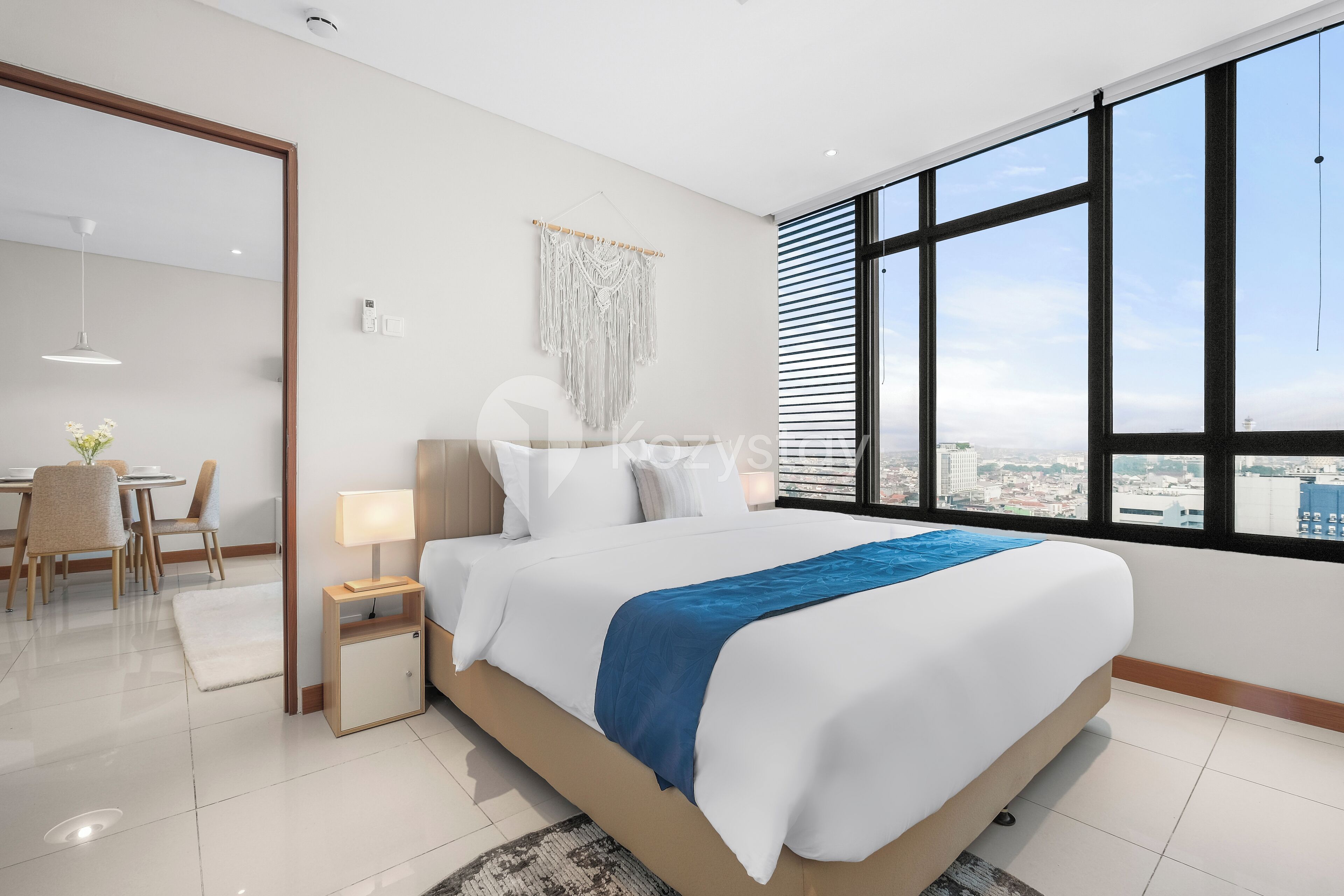 A modern hotel room with a large bed, a view of the city, a dining area, and a small seating space.