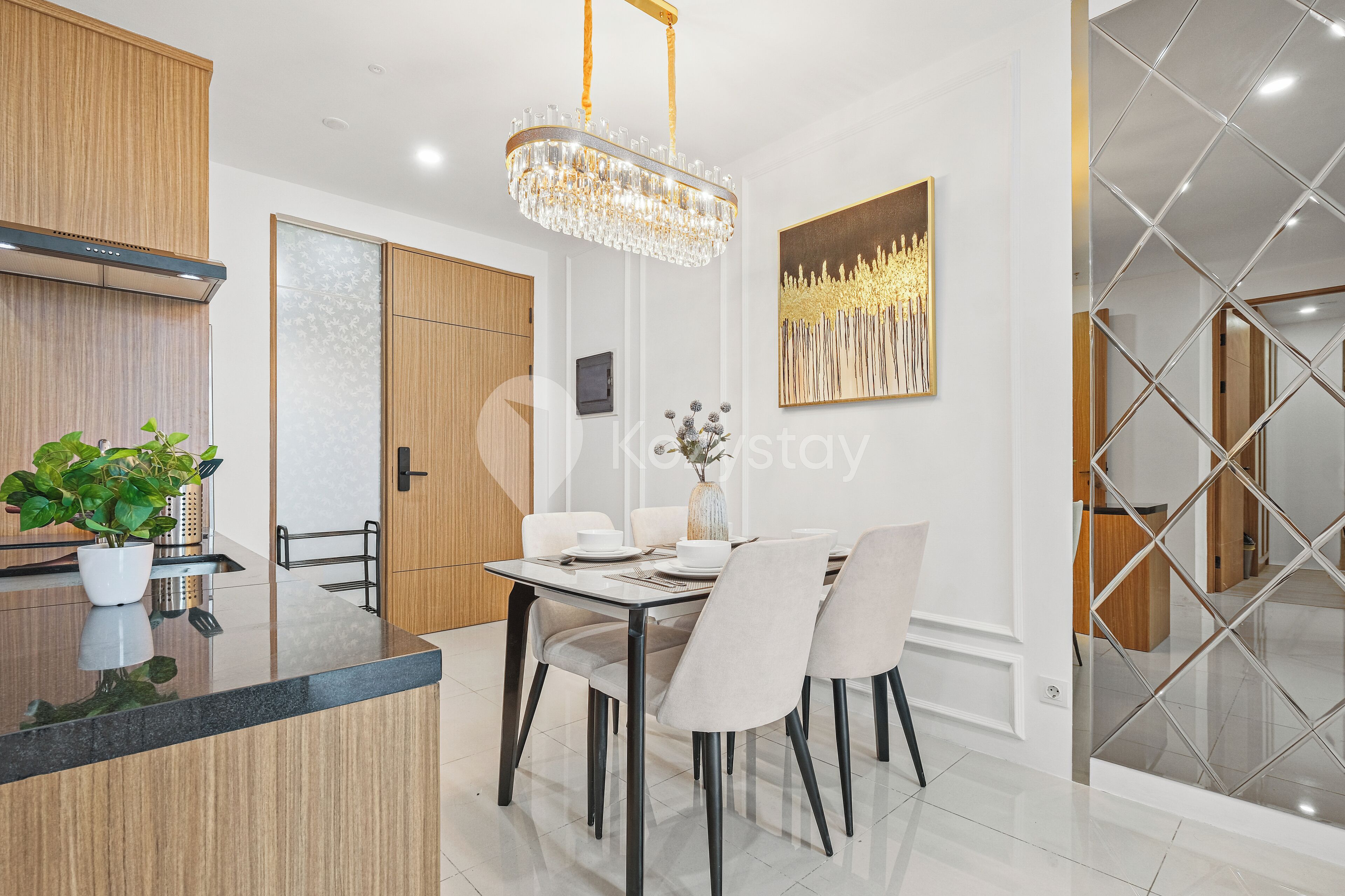A modern kitchen with wooden cabinets, a black countertop, and a chandelier. There is a dining table with chairs and a vase with flowers.